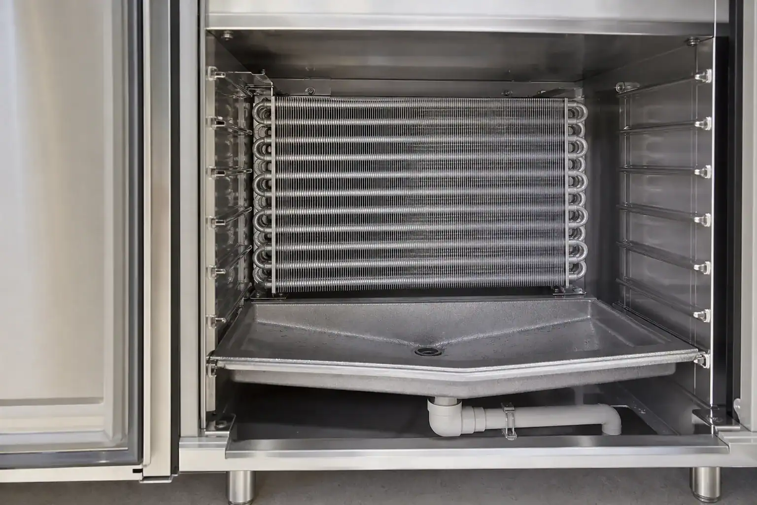 Interior view of a commercial refrigeration unit with cooling coils and drainage system.