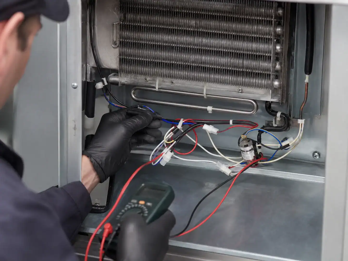Technician checking defrost wiring beneath a commercial refrigerator evaporator coil