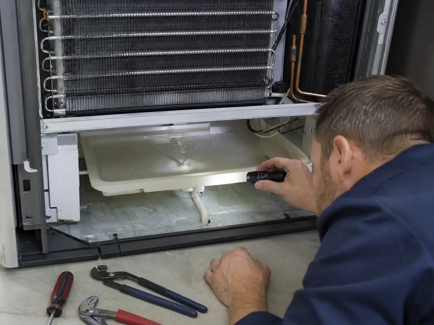 Technician inspecting a refrigerator evaporator drain pan after defrost