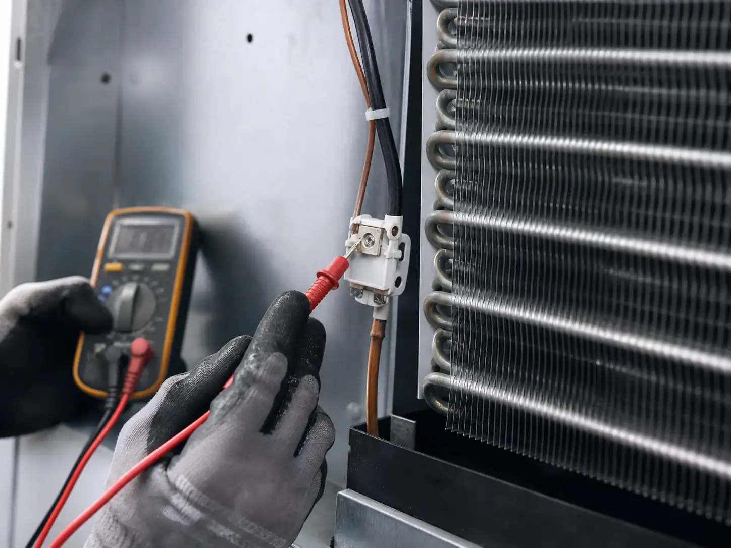 Technician testing a defrost thermostat beside a refrigeration evaporator coil
