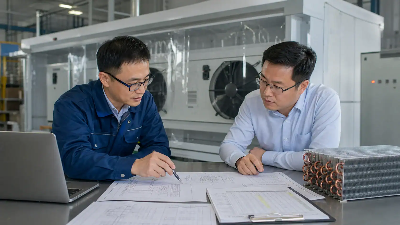 Two technicians discussing refrigeration system plans in a factory.