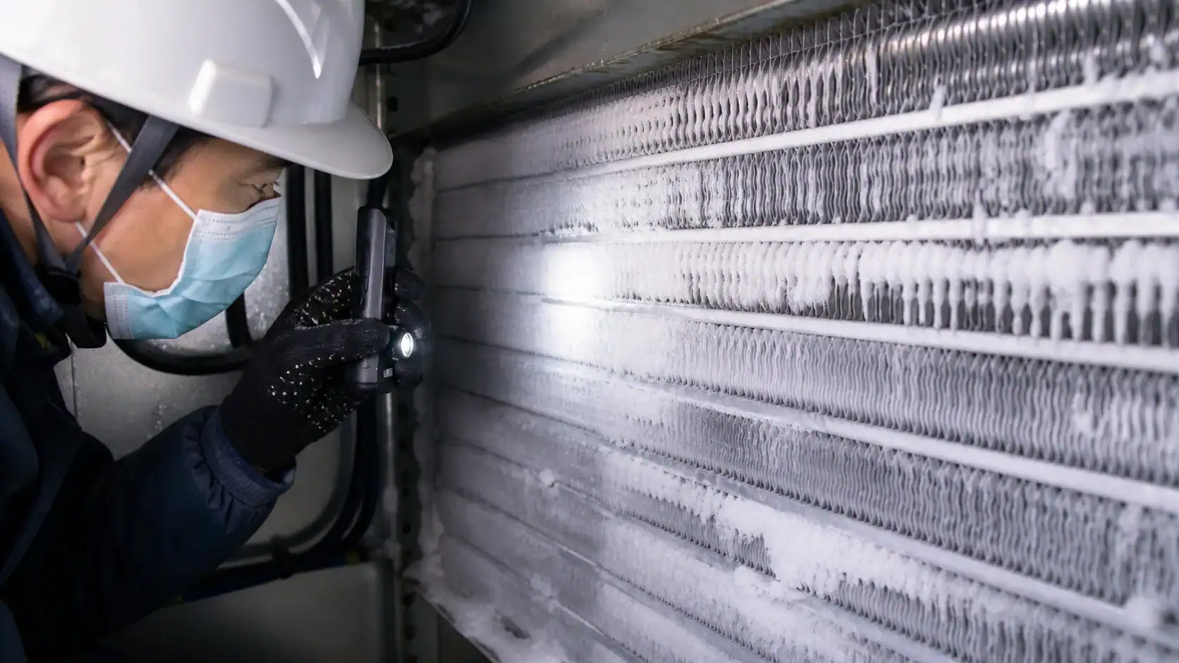 Technician inspecting industrial refrigeration unit with ice buildup.